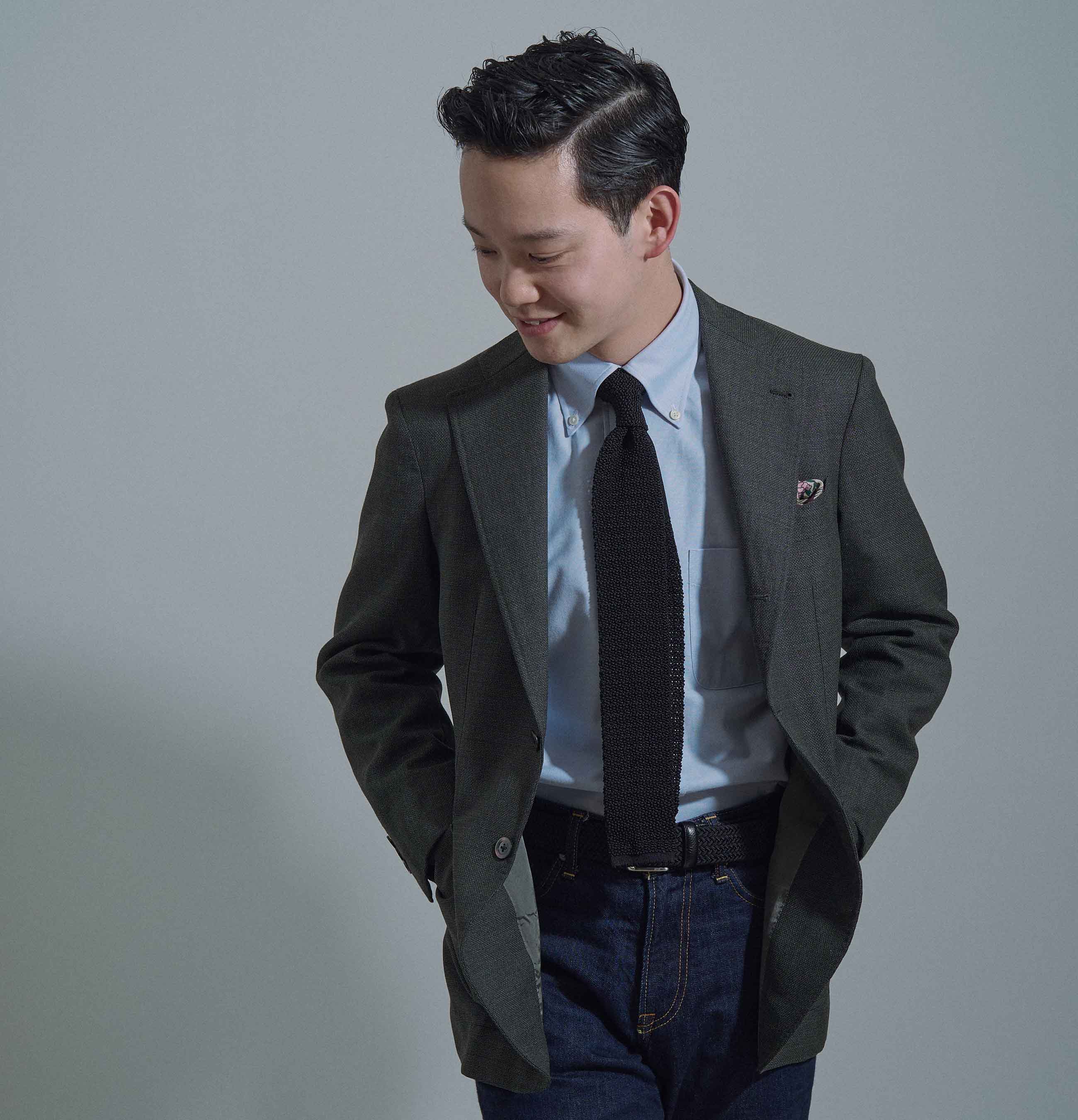 A man in a blazer and tie poses with hands in pockets.