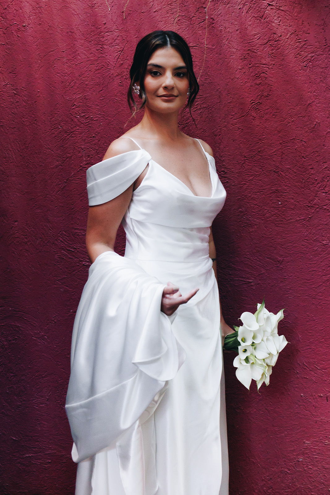 Bride in a white gown holding a bouquet, standing against a pink background.