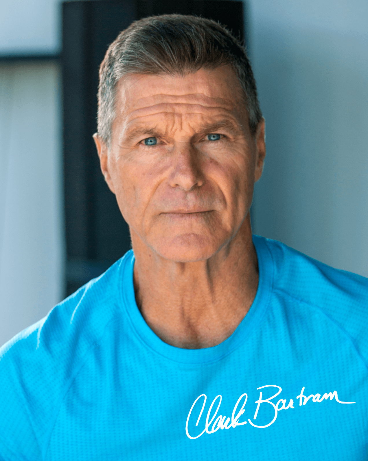 Man in a blue shirt with short hair, serious expression, and signature.