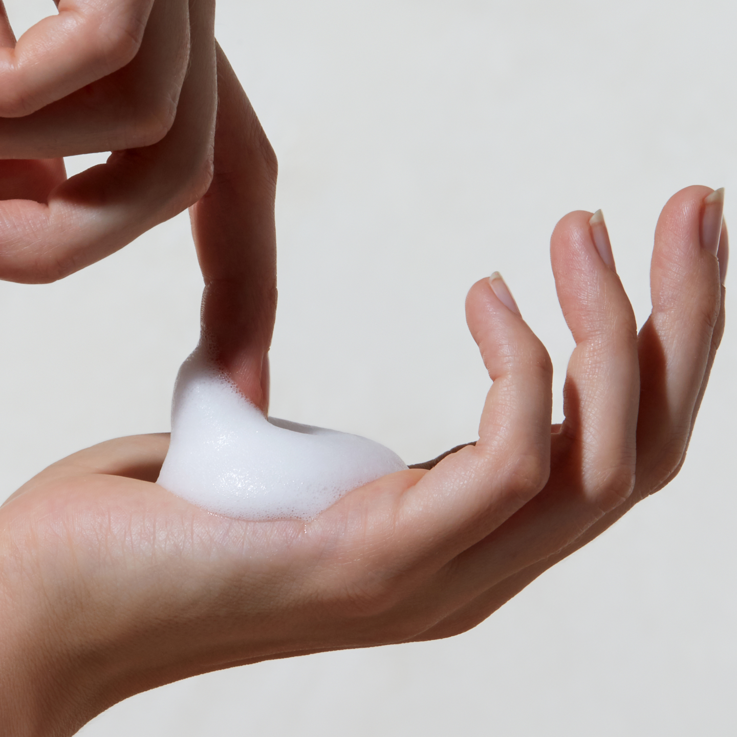 A hand holding a foam substance against a light background.