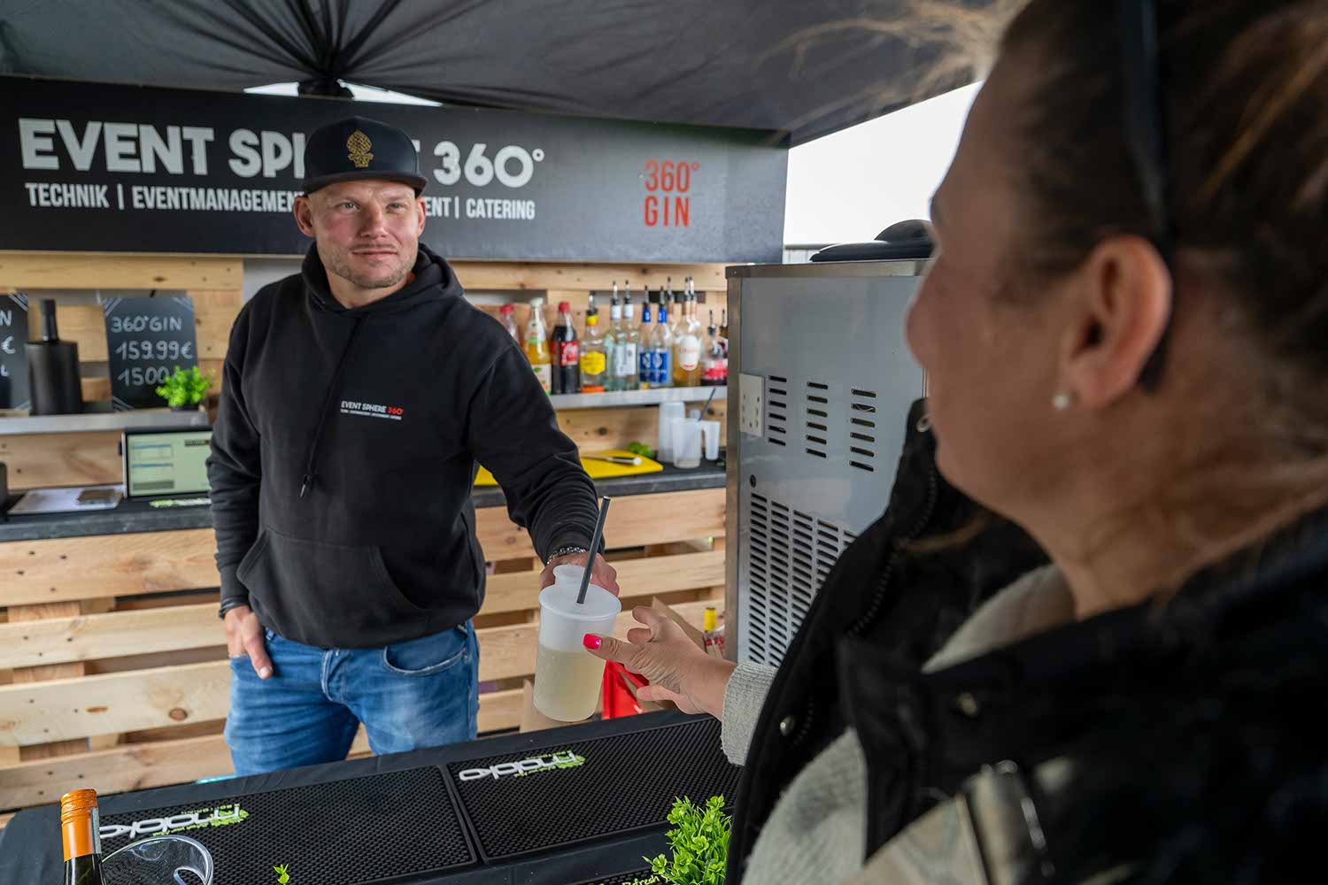 Man serving a woman at an outdoor event booth.