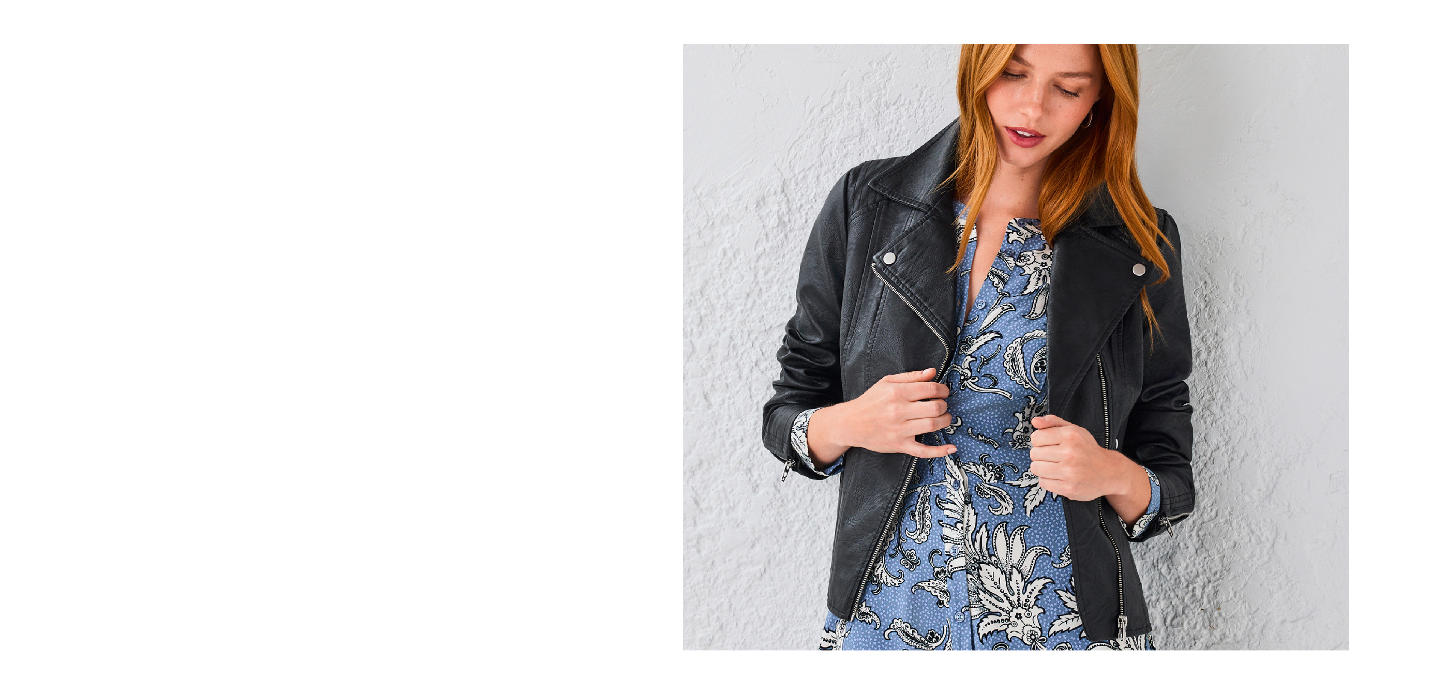 Woman wearing a black jacket over a floral dress, standing against a light background.