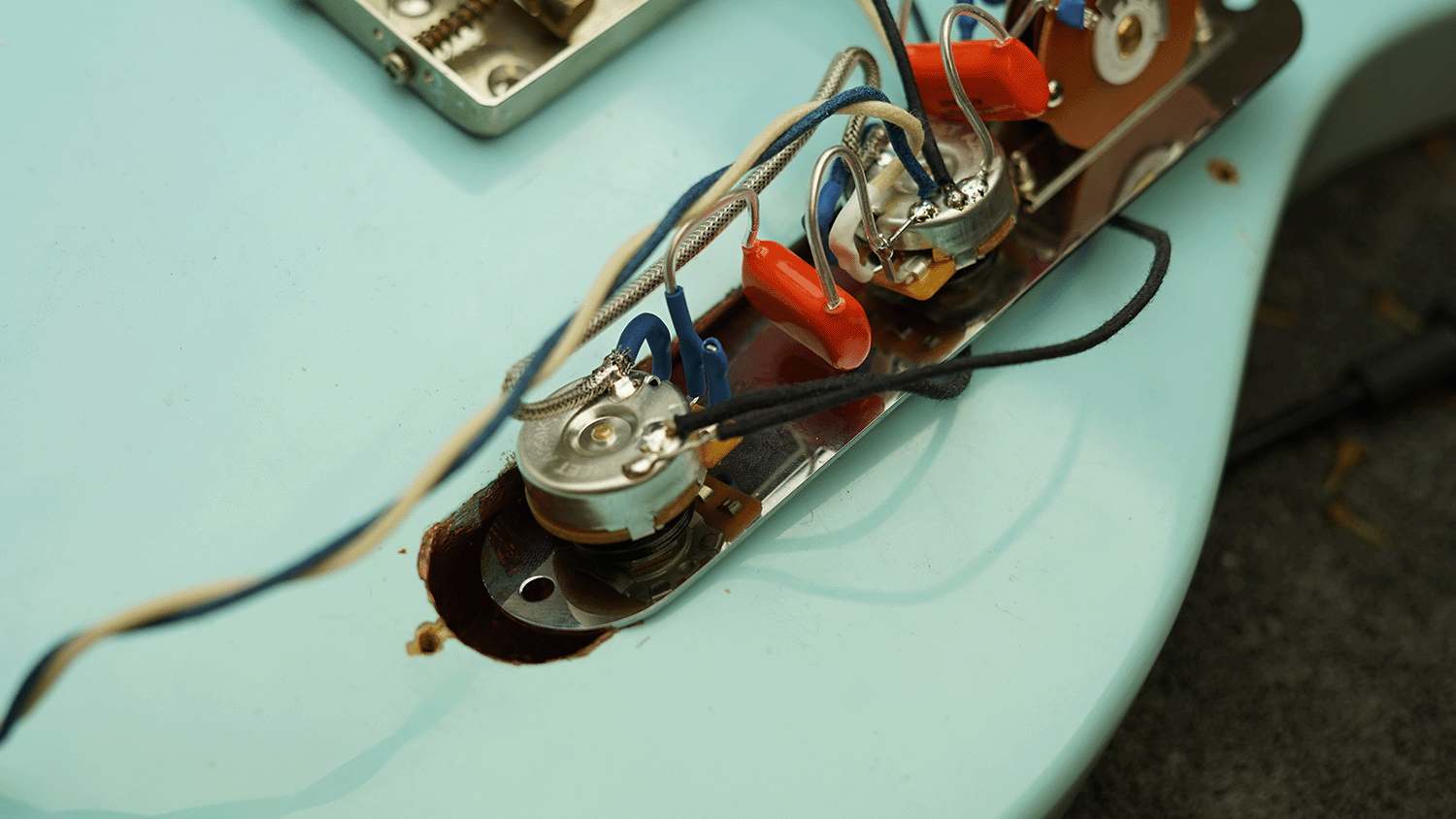 Close-up of guitar wiring and components on a light blue guitar body.
