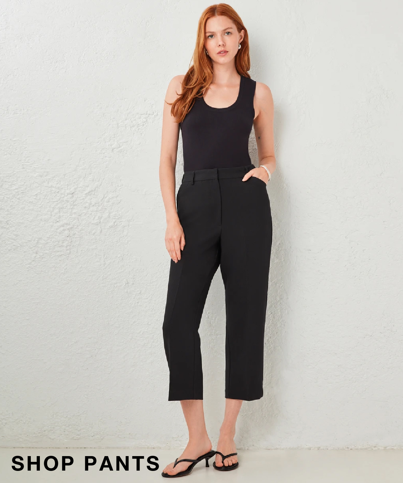 Woman in black pants and tank top standing against a light background.