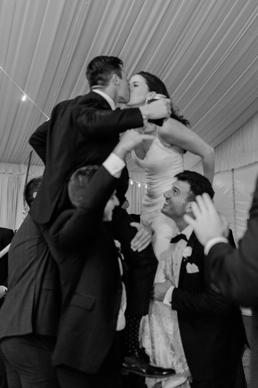 Couple celebrating at a wedding, lifted by friends in formal attire.