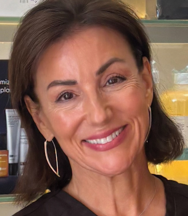 Smiling woman with short brown hair and hoop earrings in a beauty setting.