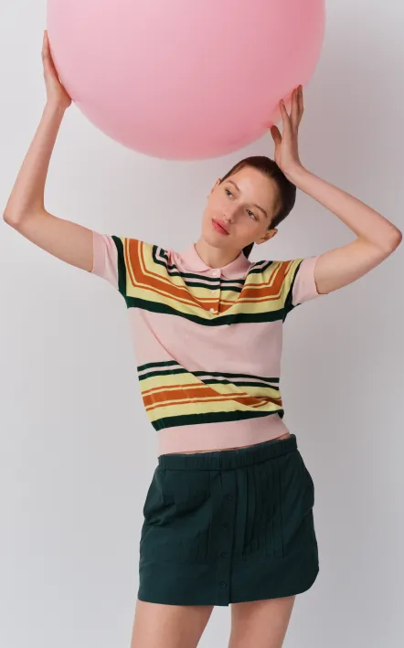 Woman holding a large pink balloon, wearing a colorful striped shirt and shorts.