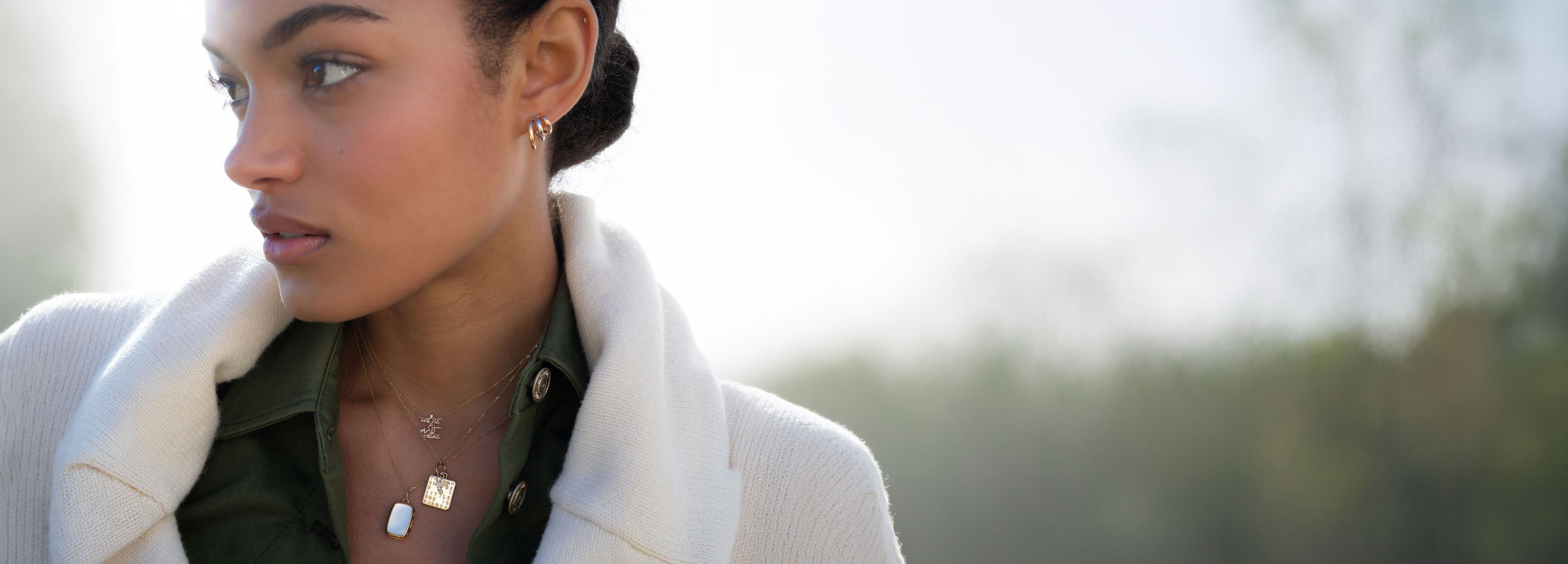 Woman with earrings wearing a white coat, looking away outdoors.