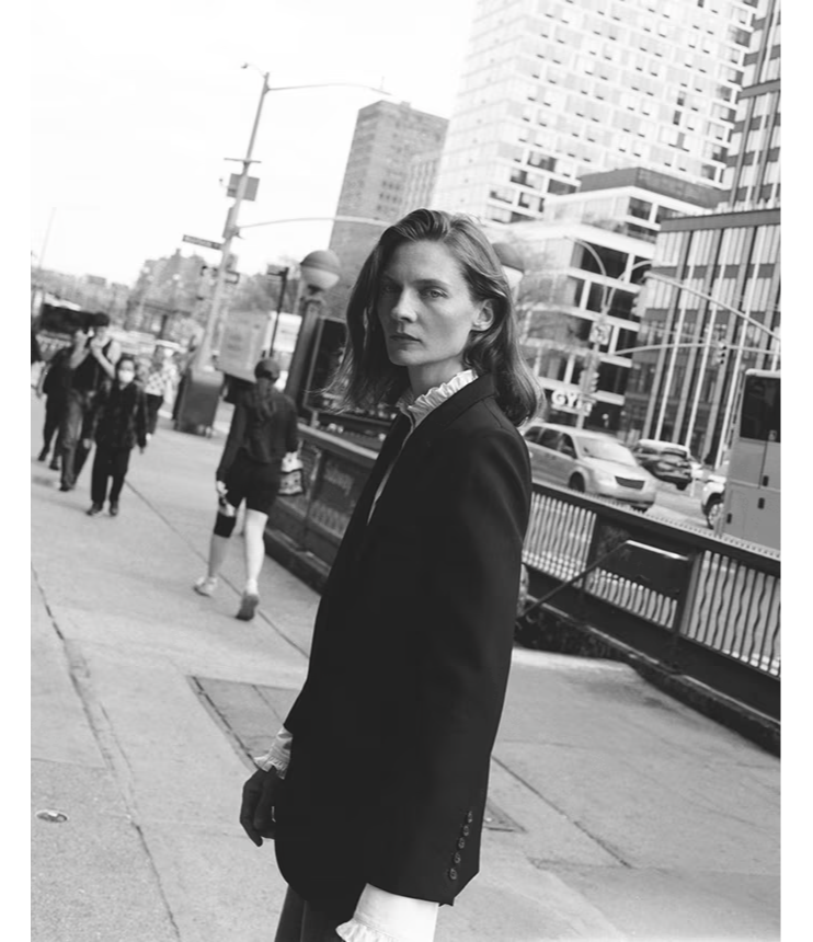 A person in a black suit walking in a city street.