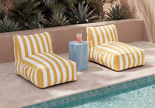 Two striped lounge chairs beside a pool, with a blue table and drink.