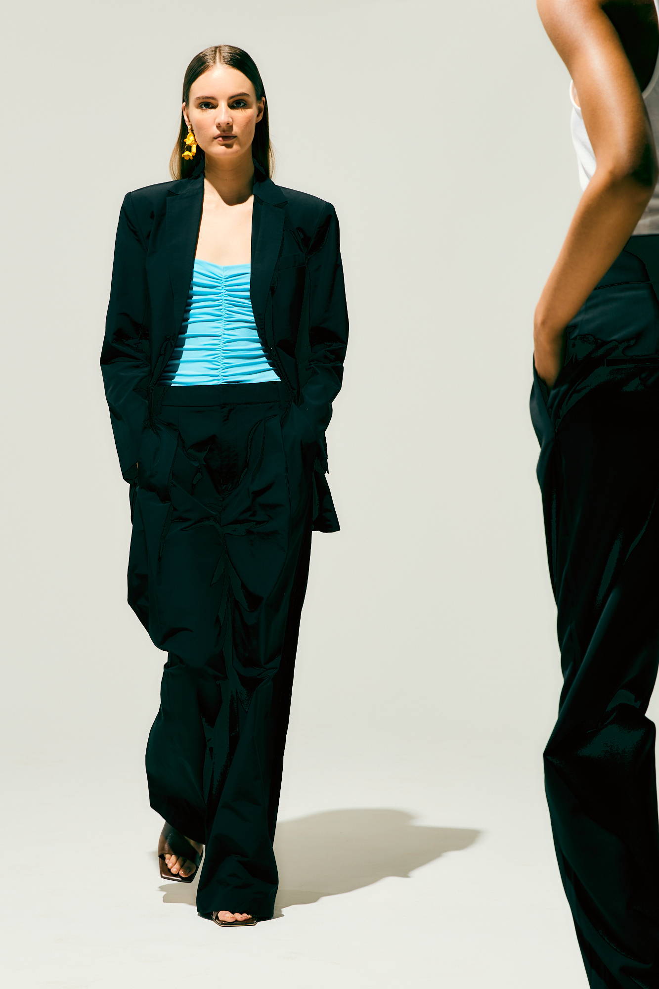 Model in stylish outfit, featuring a blazer and striped top, on a plain background.