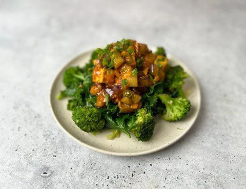 Plate of sautéed tofu on a bed of broccoli and greens.