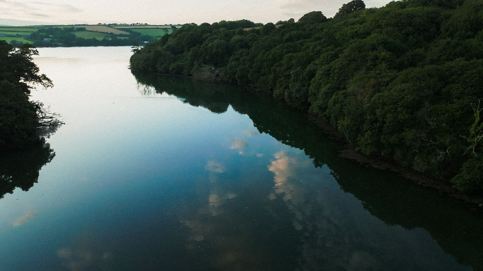 A serene river surrounded by lush green trees and reflected clouds.