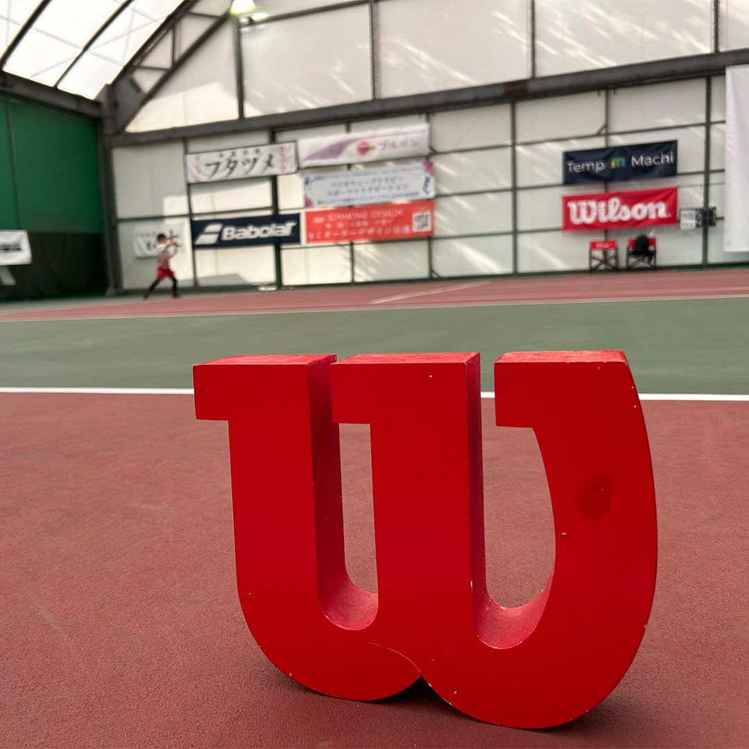 Red Wilson logo in a tennis court setting.