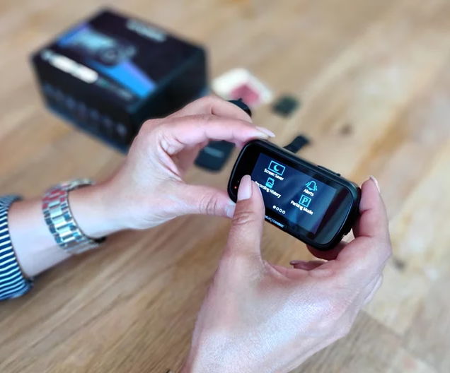 Person holding a Nextbase dash cam displaying its touchscreen settings menu.