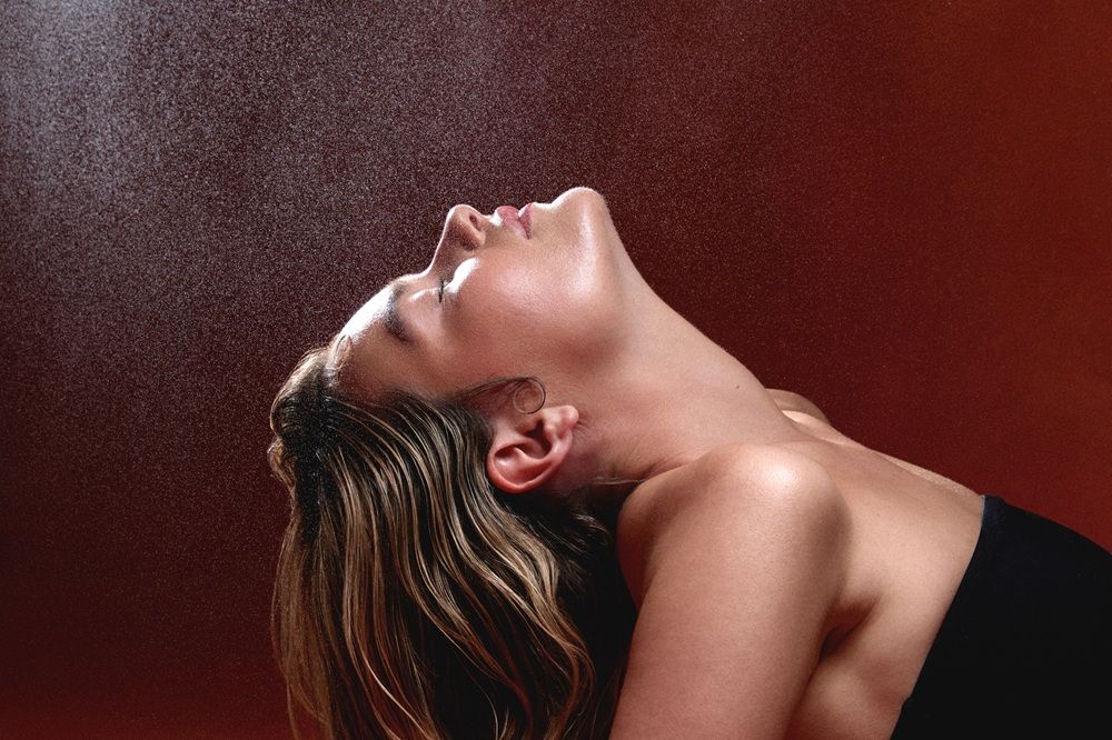 Woman with tilted head against a textured backdrop, light reflecting on her skin.