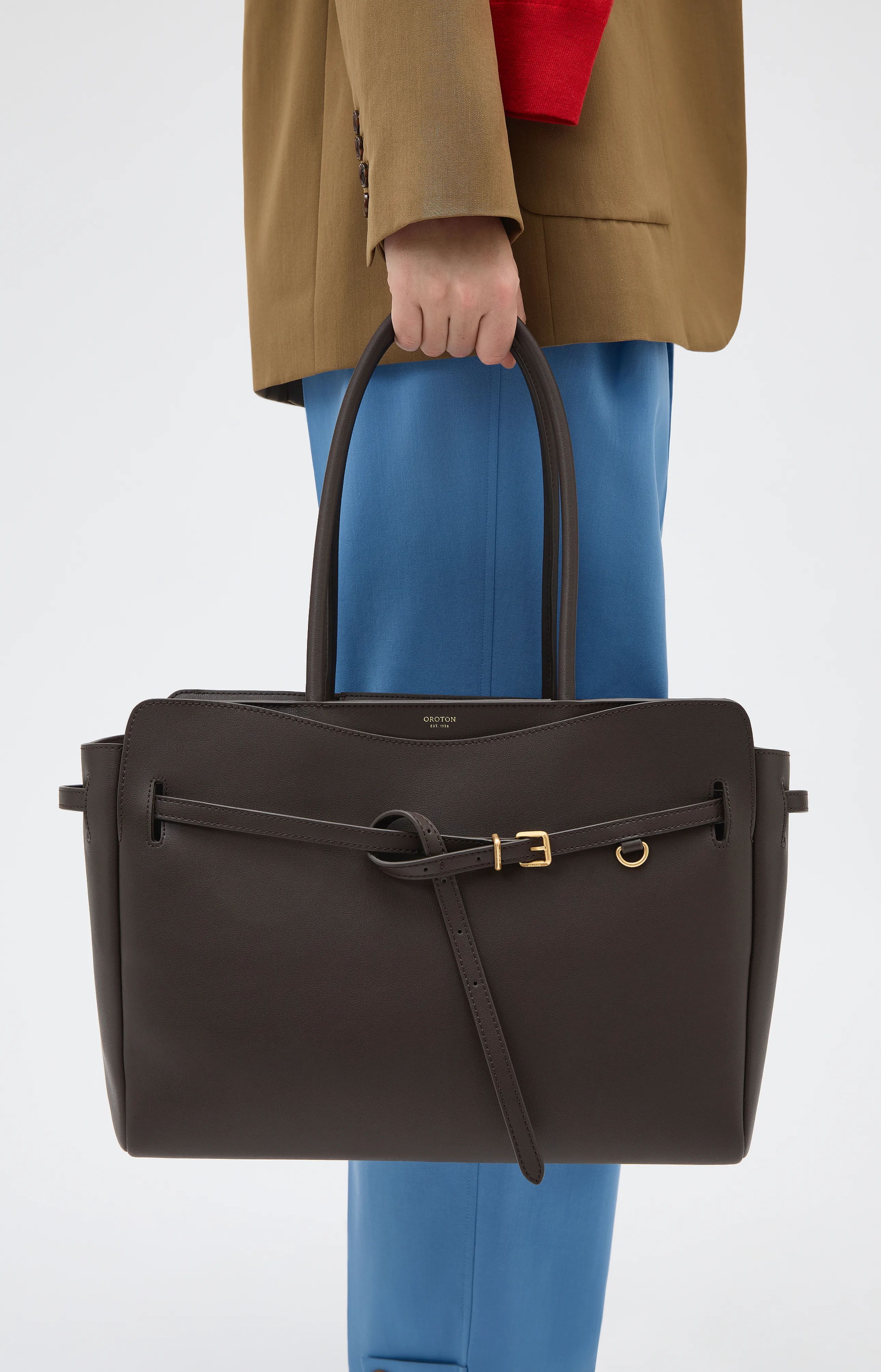 Person holding a large brown handbag, wearing a blazer and blue pants.