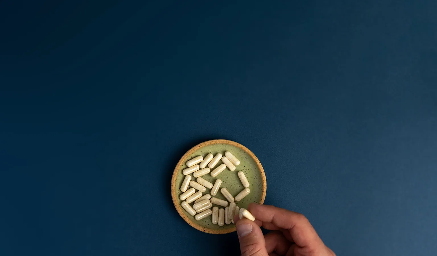 A shallow green bowl with a couple dozen Neuralli MP capsules in the bottom. A hand is grabbing one of the capsules.