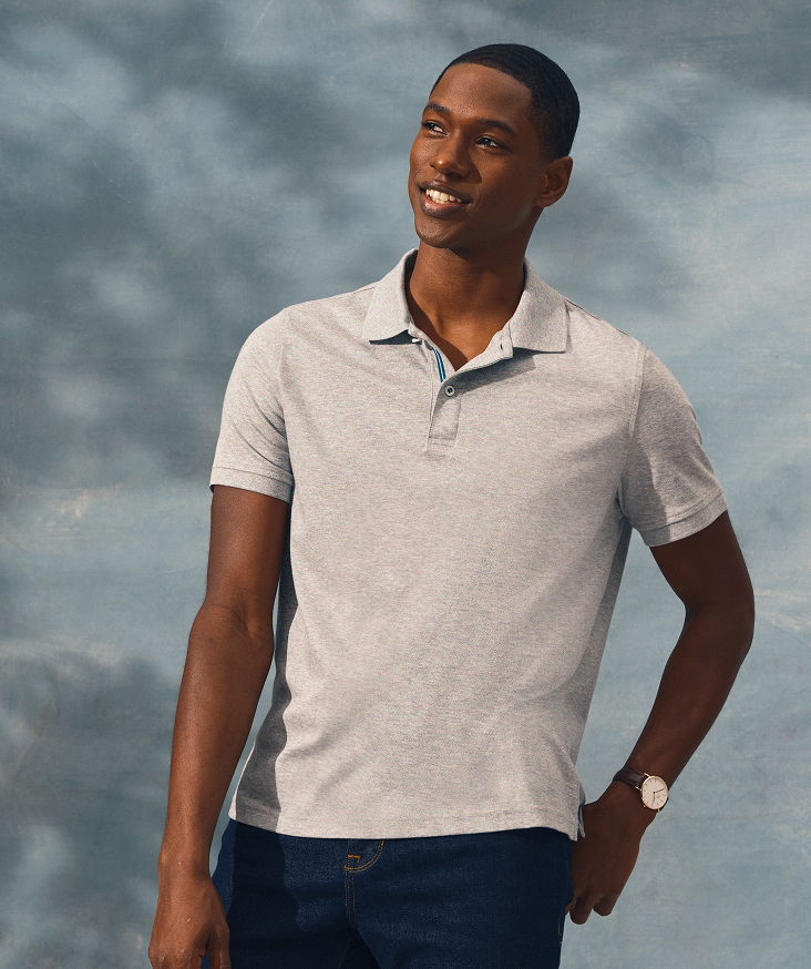 Smiling man in a gray polo shirt against a cloudy background.