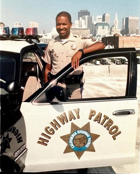 A police officer standing by a marked patrol car in a city.