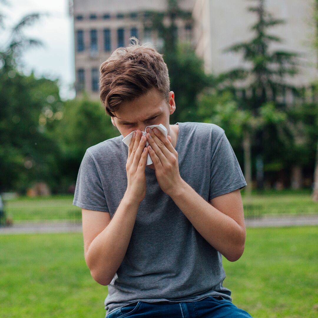 Mladý muž v parku smrká - má upchatý nos a zároveň mu tečie z nosa kvôli alergickej nádche