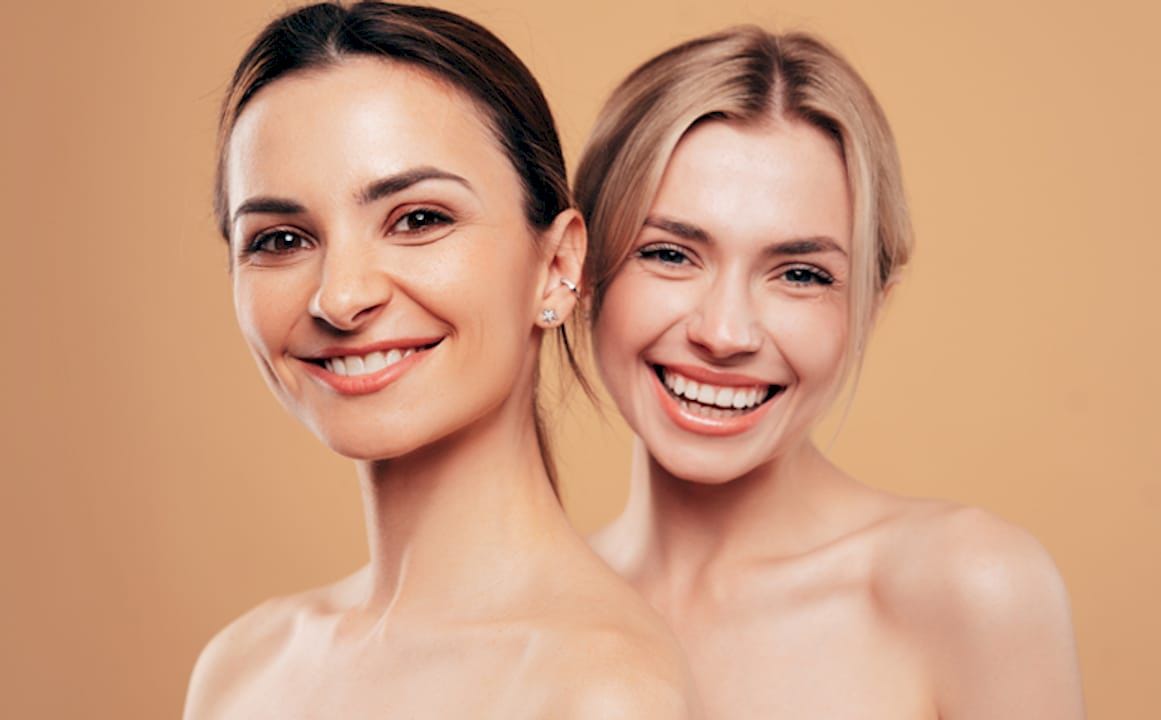 Two smiling women with natural makeup against a beige background.