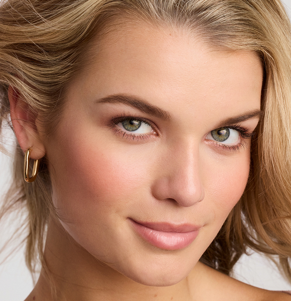Close-up of a young woman with wavy hair and earrings, smiling.