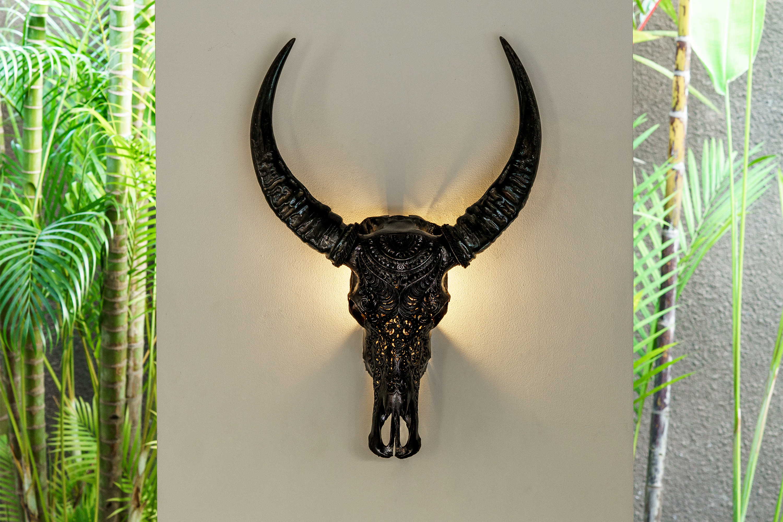 The Carved Buffalo Skull Lamp 'Black Boho' is hanging on a wall.