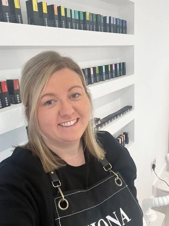 Smiling woman in an apron stands in front of nail polish display.
