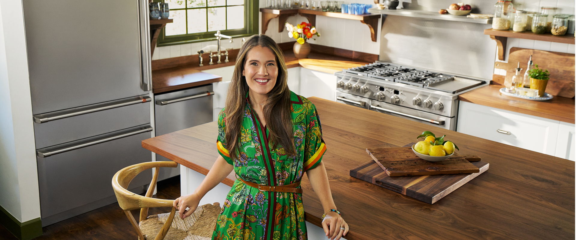 Person smiling in a colorful dress, standing in a modern kitchen.
