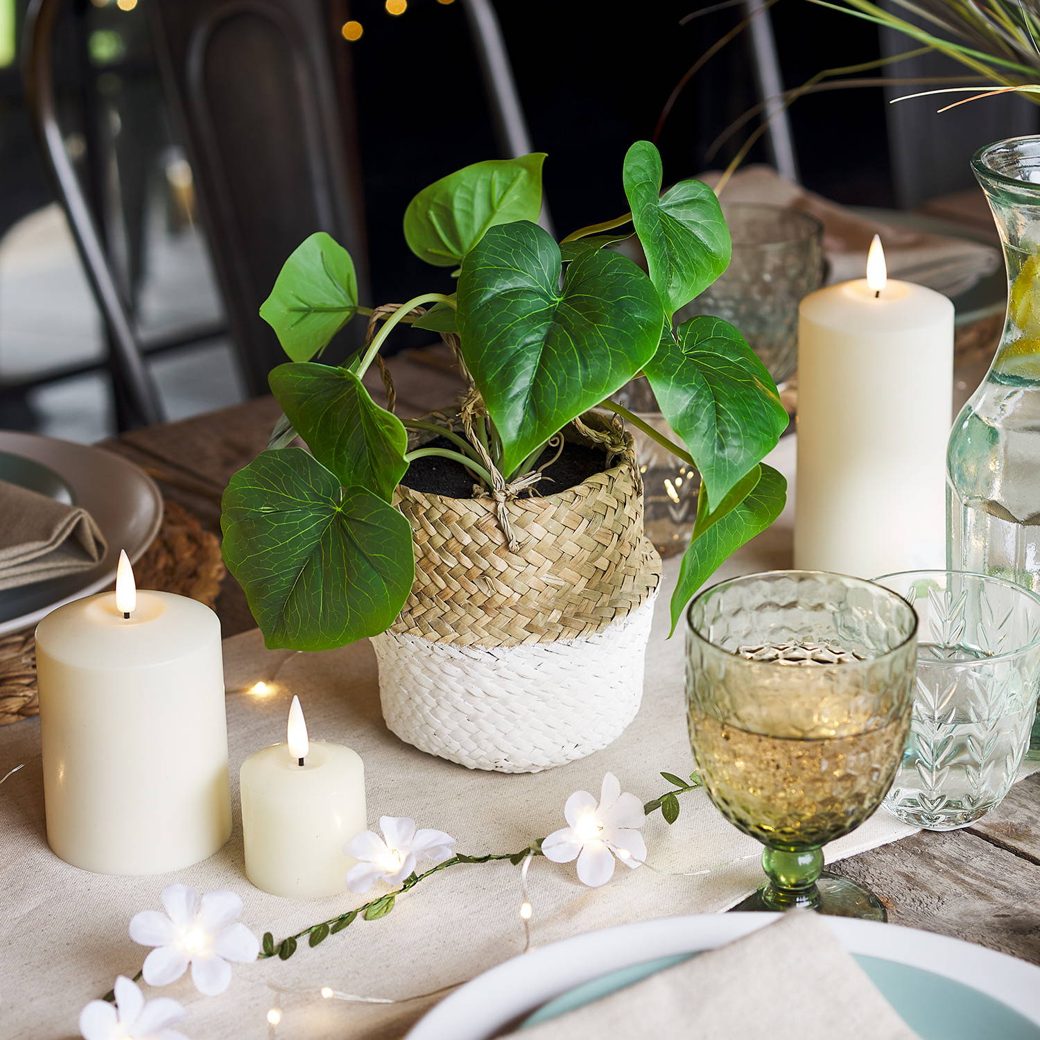 An alfresco dining set up with a faux plant, candles, a flower garland and drinks.