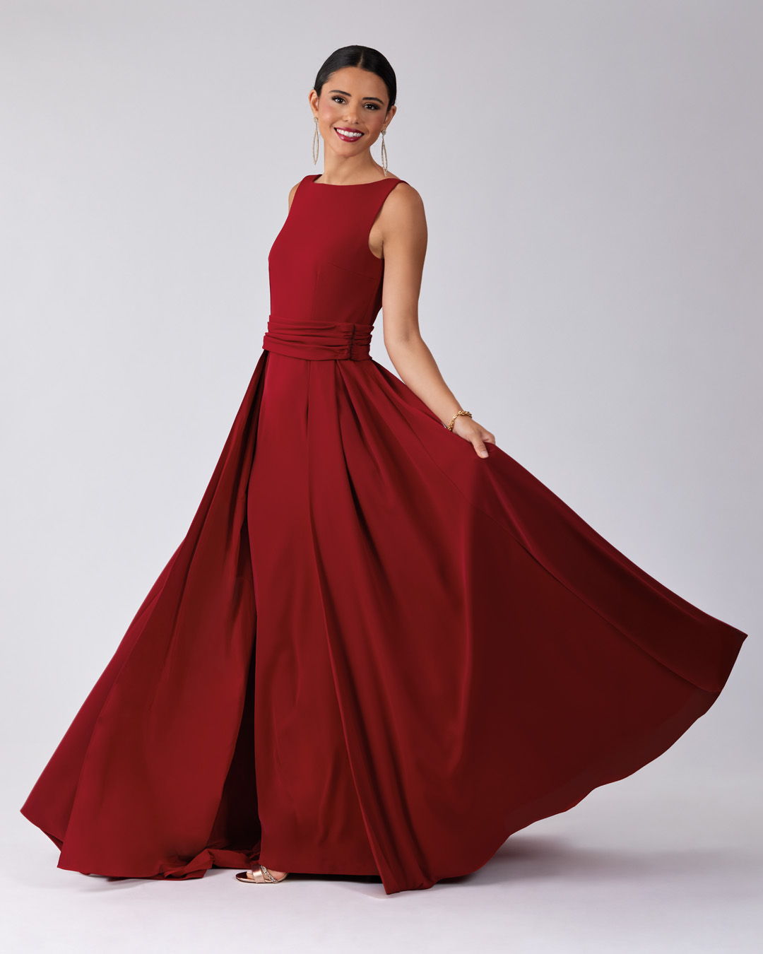 Woman in a flowing burgundy dress, smiling and posing against a neutral background.