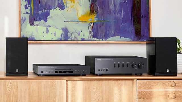 Audio equipment on a wooden shelf with abstract art in the background.