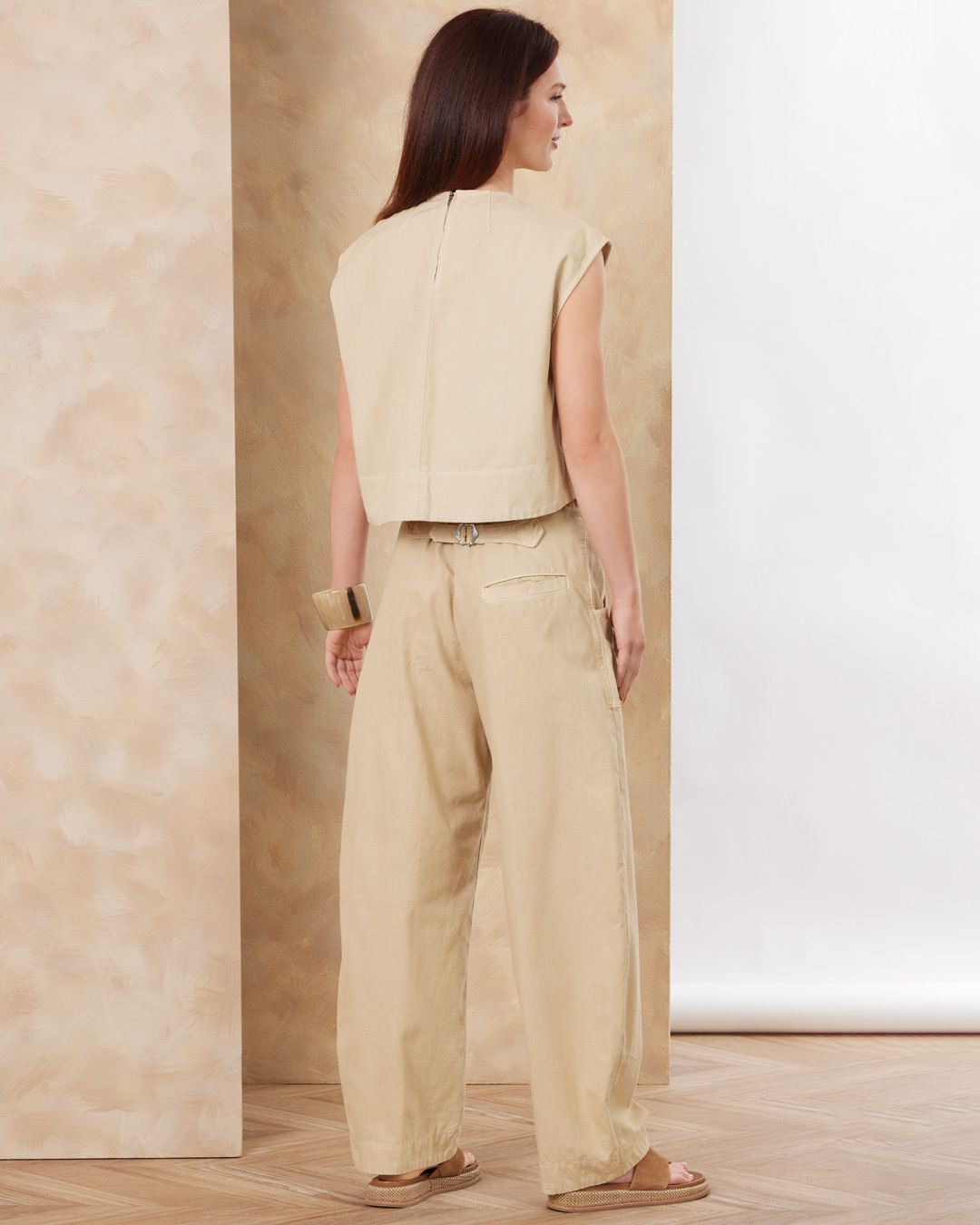 A woman in beige clothing stands against a neutral background.