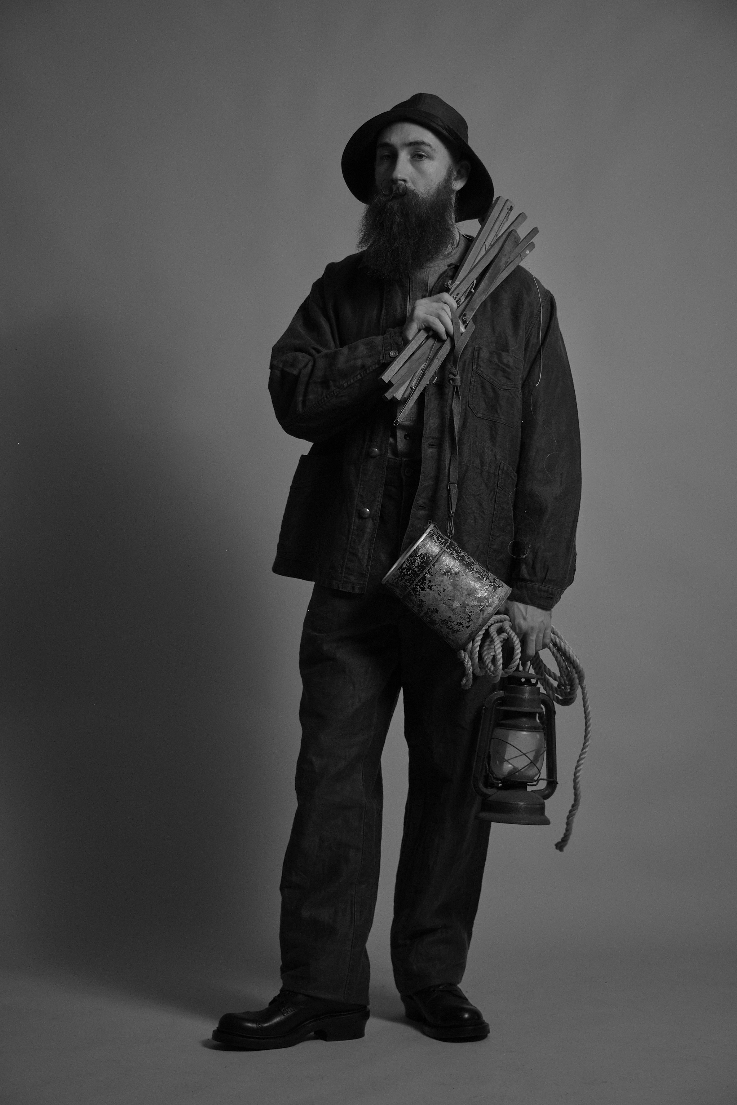 A man in a black and white photo holding sticks and a lantern.