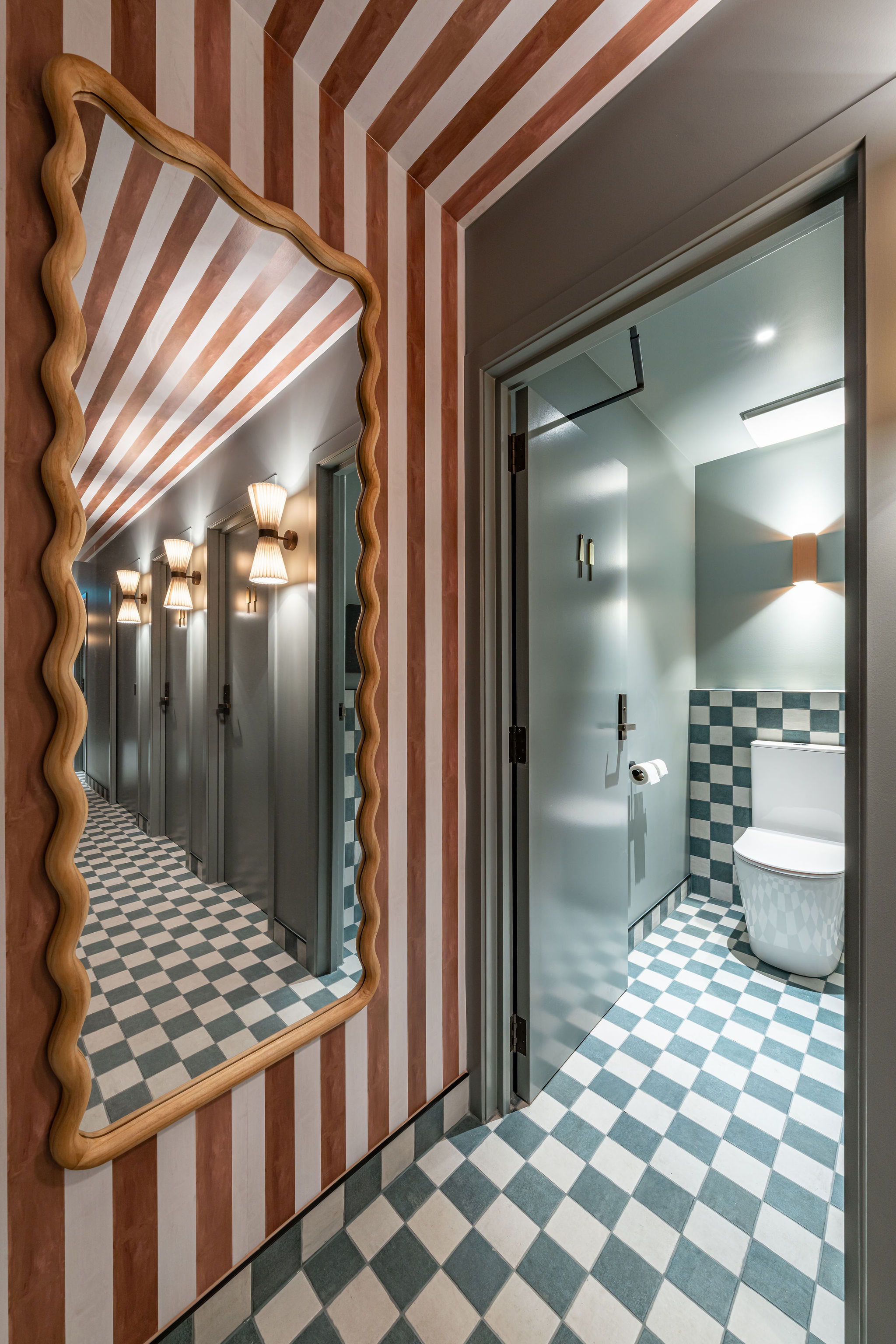 Modern bathroom with striped walls, checkered floor, and decorative mirror.