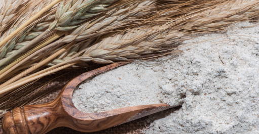 Wooden spoon of flour with wheat lying next to it