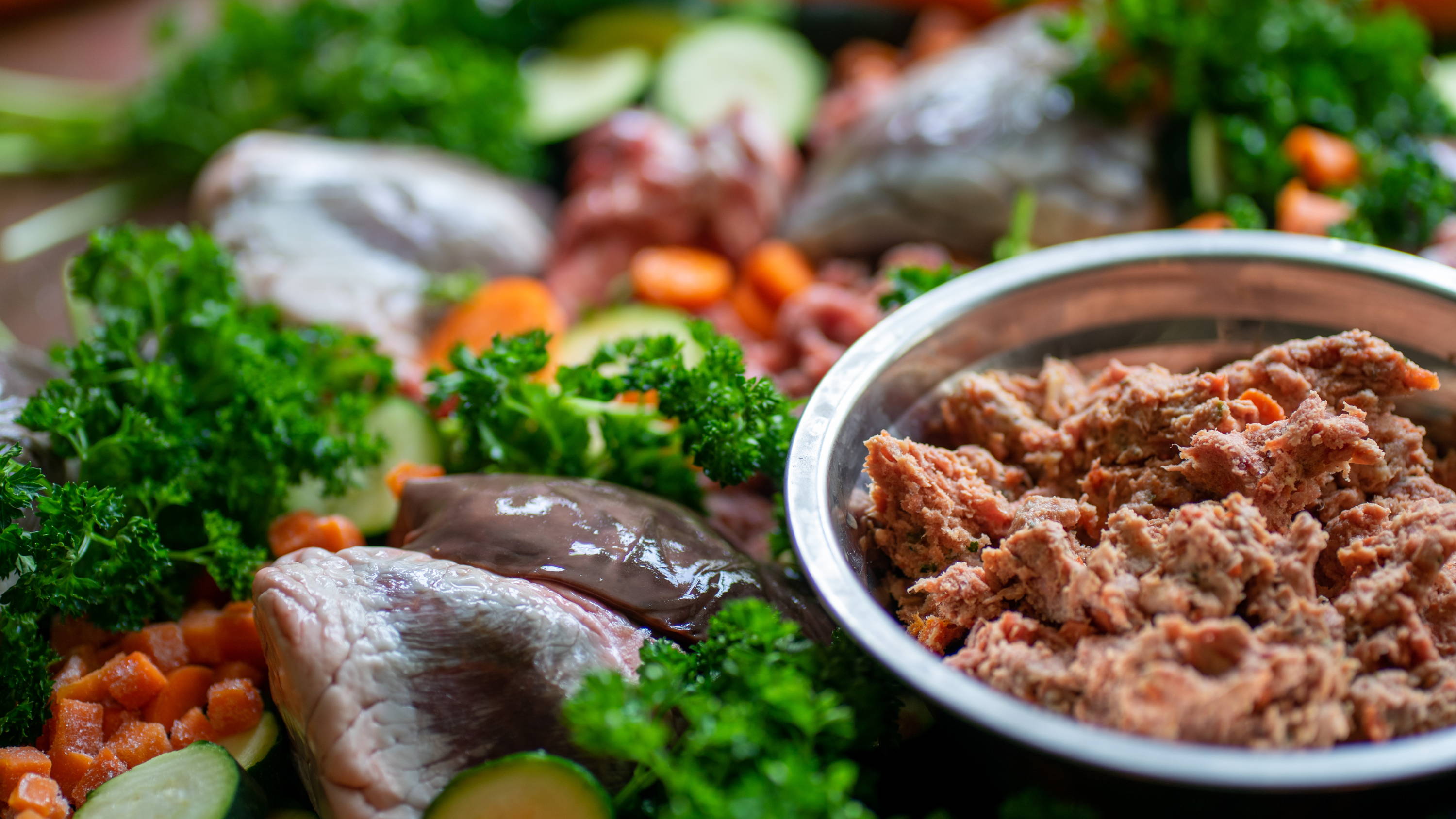 Ground lamb meat in silver bowl on top of raw meat and vegetables.