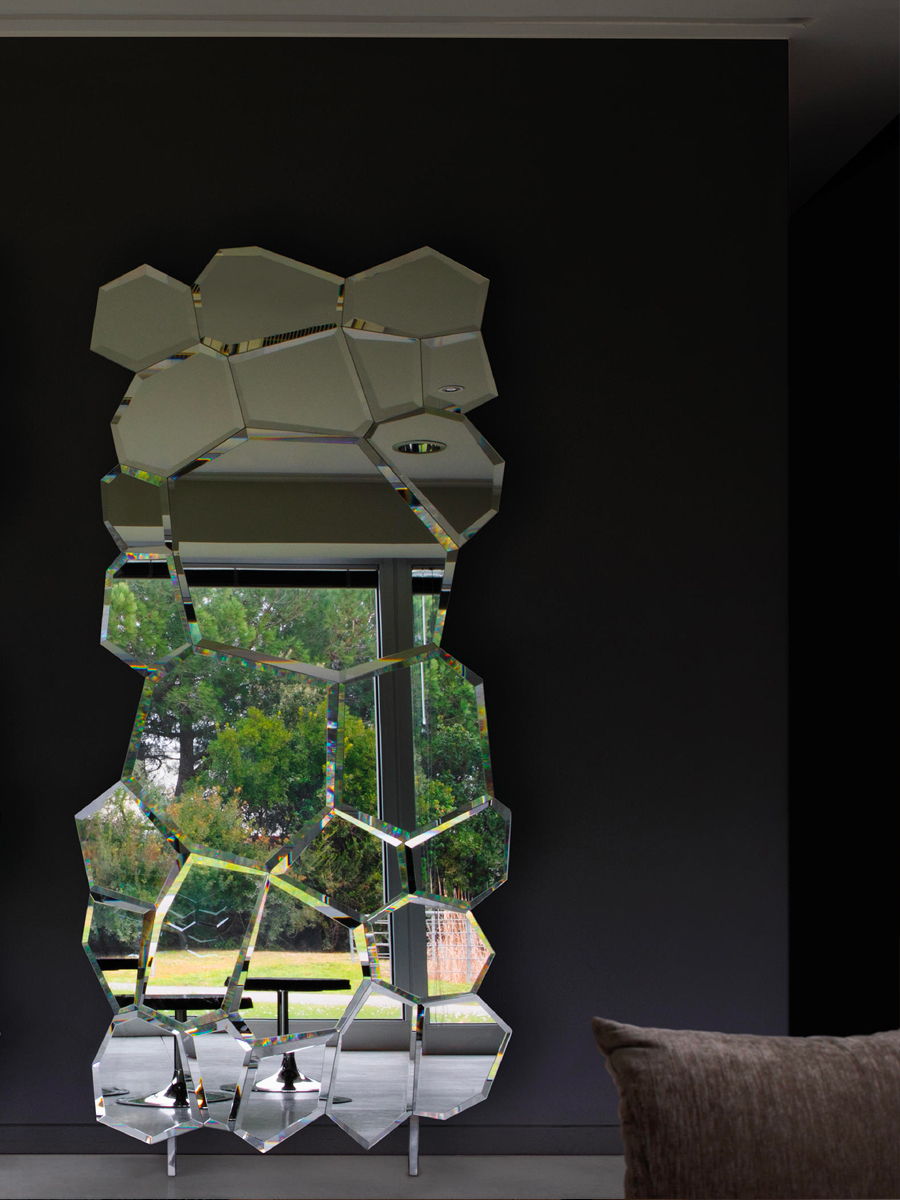 Unique hexagonal Jubile mirror by Edra reflecting greenery in a modern interior setting.