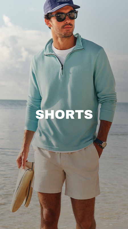 Man wearing a light blue pullover and shorts by the beach.