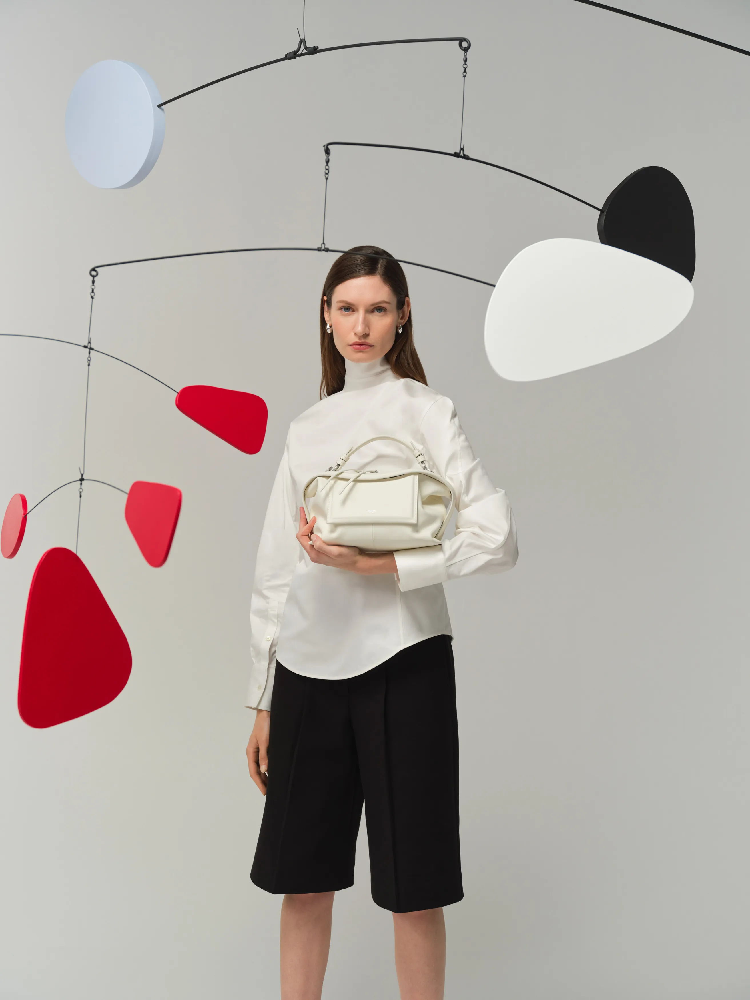 A model in a white blouse holds a handbag against a minimal background.