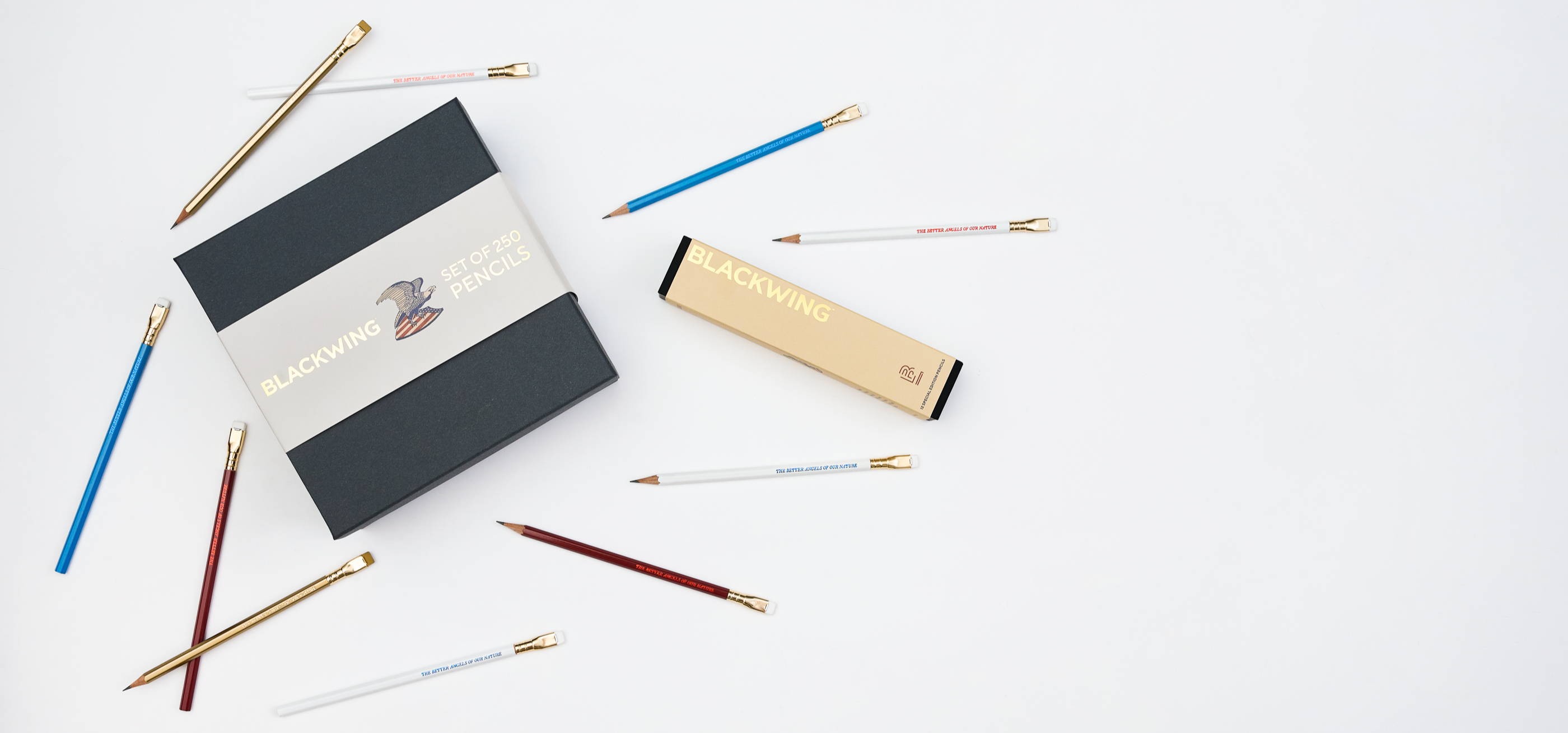 several Blackwing 250 pencils in red, white, blue, and gold shown on a white background next to the bulk set of 250 packaging and a 12-pack of pencils packaging