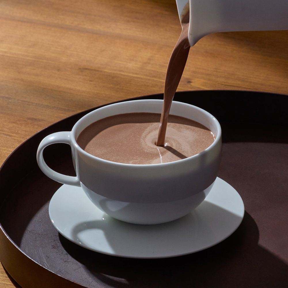A cup of hot chocolate being poured from a jug.