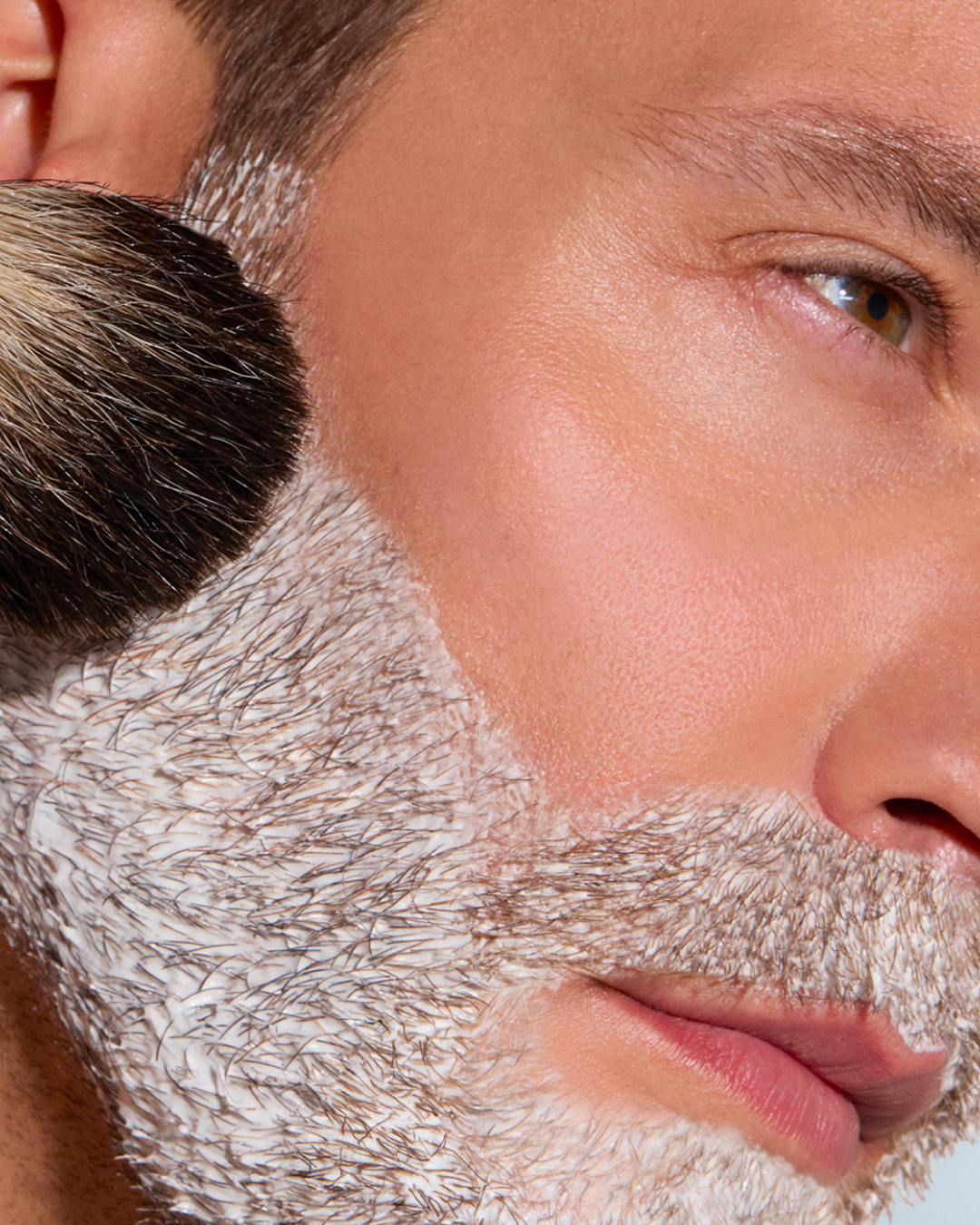 Close-up of a man applying makeup on his facial hair.