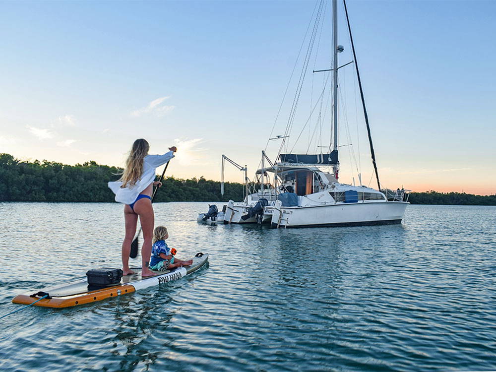 A woman with a child paddleboarding to a yacht in the keys in florida