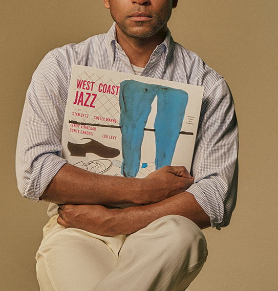 Person holding a jazz album, sitting with arms crossed, wearing a light shirt.