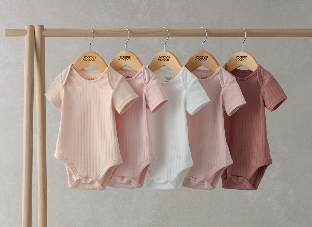 Four baby onesies in pastel colors hanging on wooden hangers.