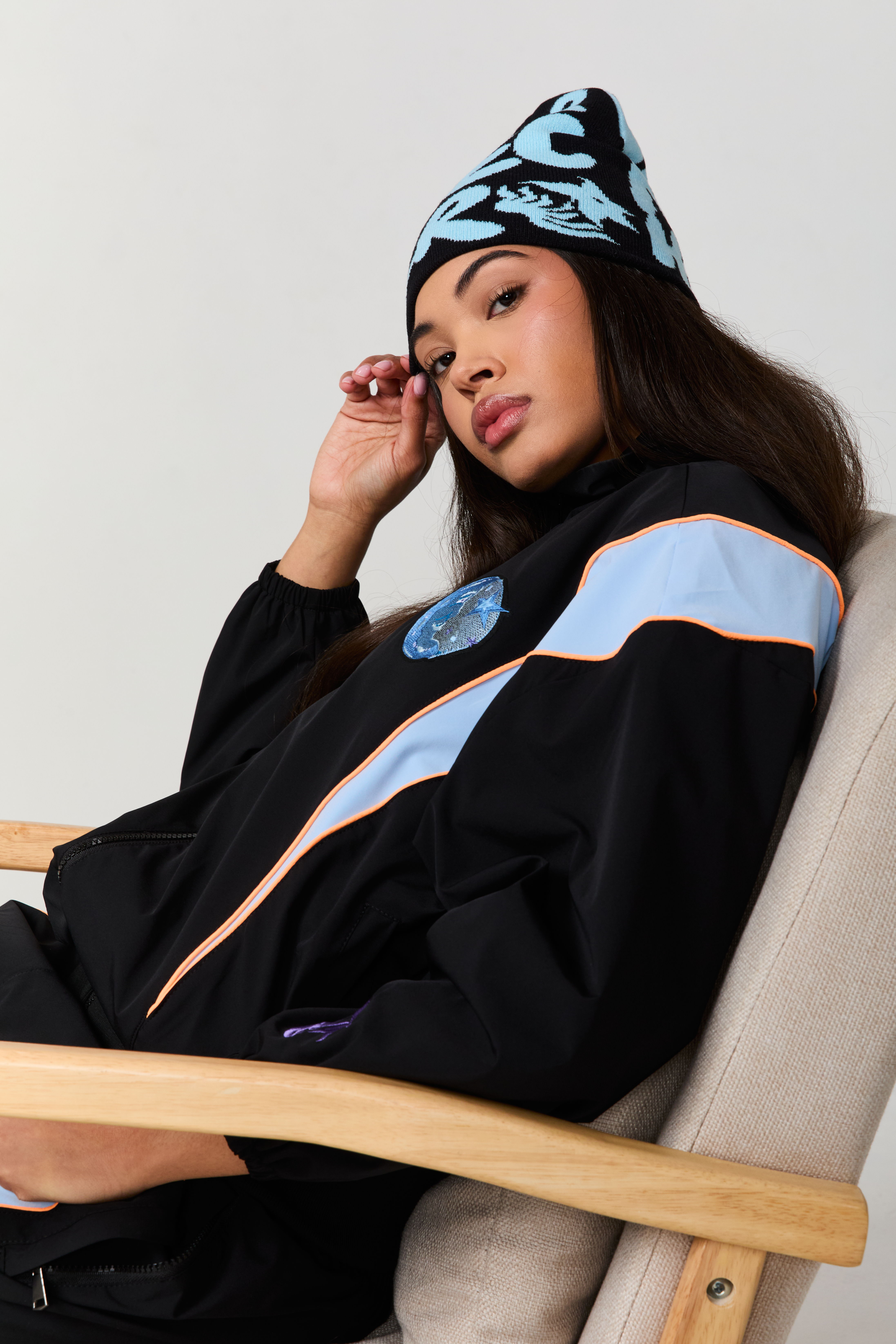 Woman in a black jacket and blue beanie sitting in a chair.