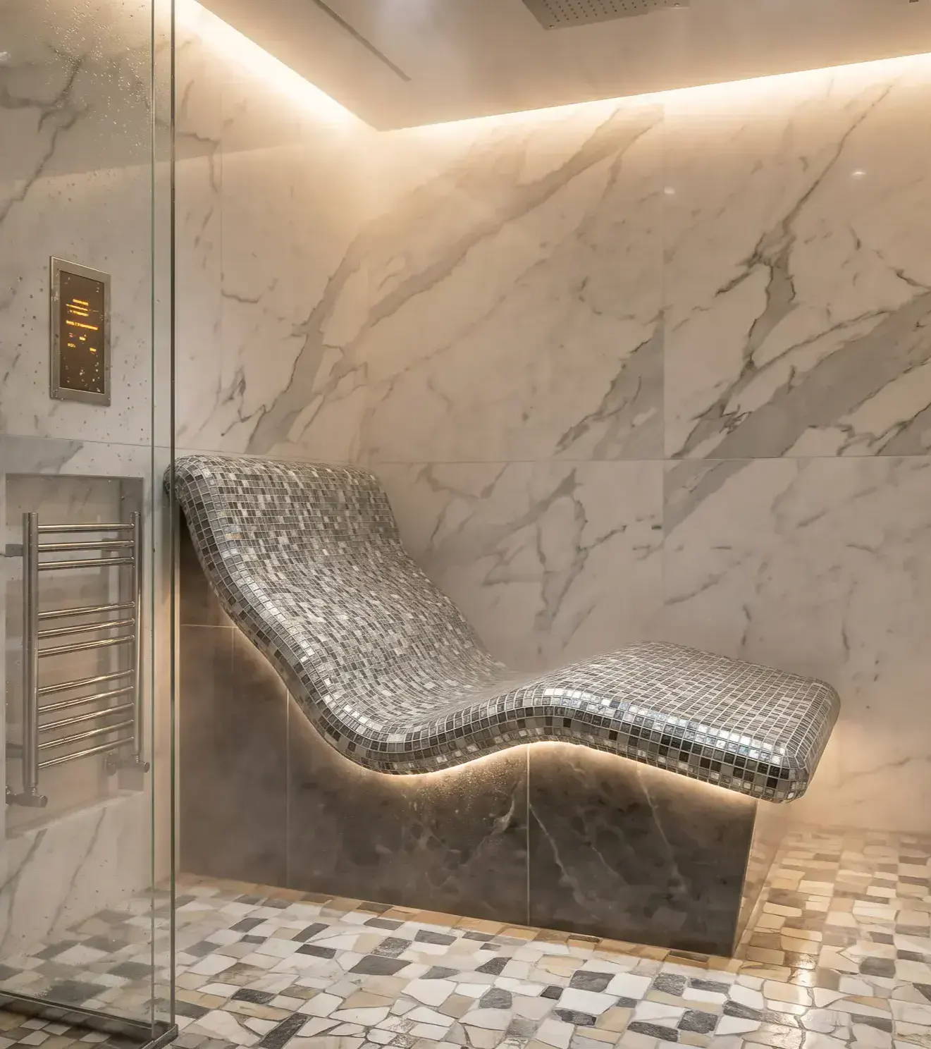 Modern tiled steam shower lounger with curved mosaic seat, marble walls, recessed ceiling lighting, and floating bench design by Custom EPS.
