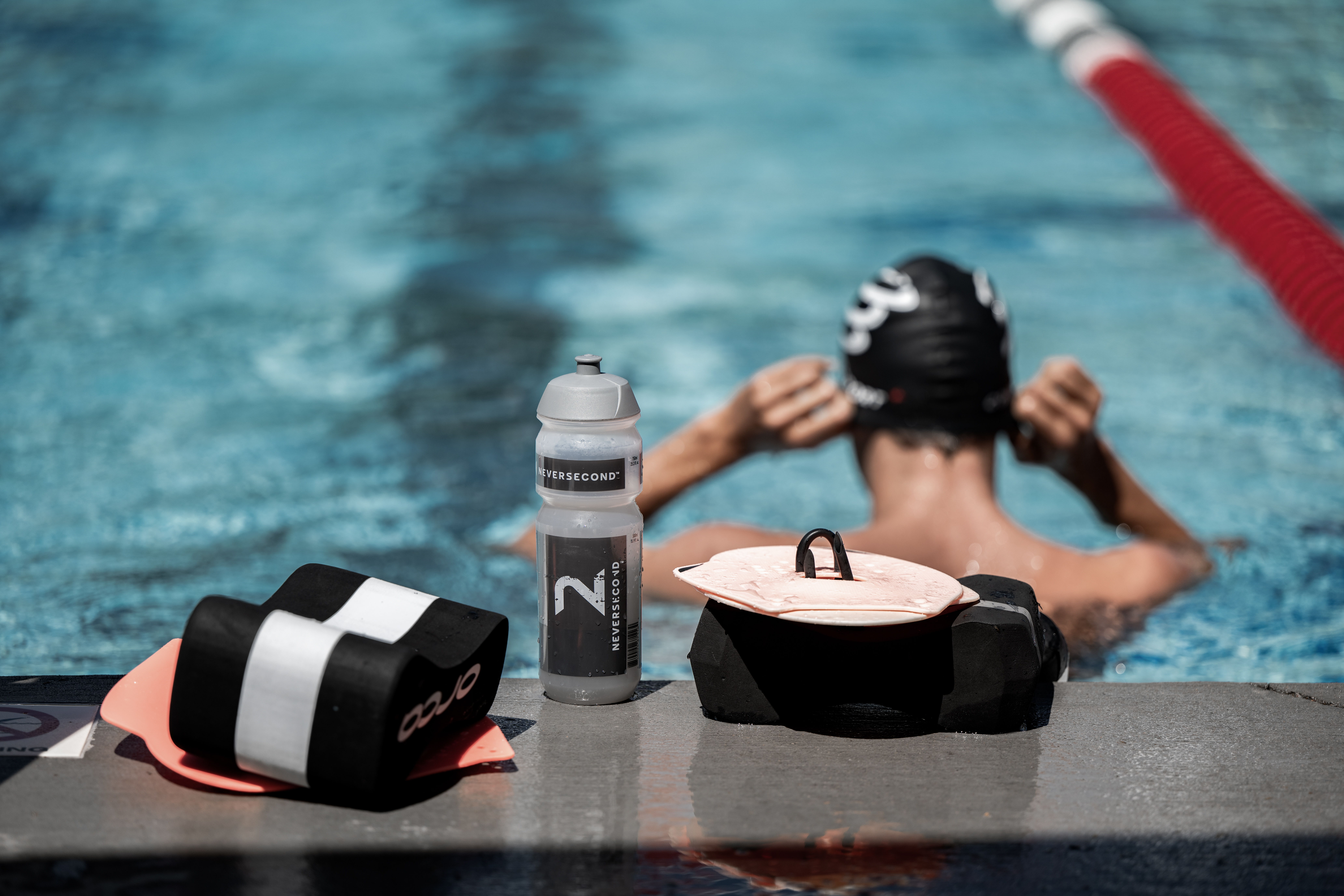 Eine Neversecond Trinkflasche eines Sportlers am Beckenrand beim Schwimmtraining.